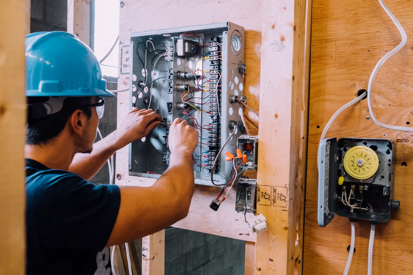 Élève en électricité, casque bleu sur la tête, qui câble un panneau